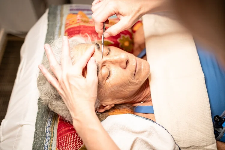 Ewa dermaplaning a client's forehead with a blade while the client rests
